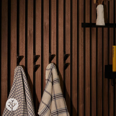Black 3D hooks installed on smoked oak Acupanel wall with patterned towels and items hanging