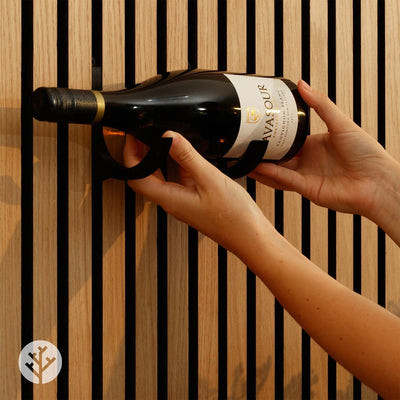 Hand placing wine bottle into black wine rack mounted on natural oak Acupanel slat wall